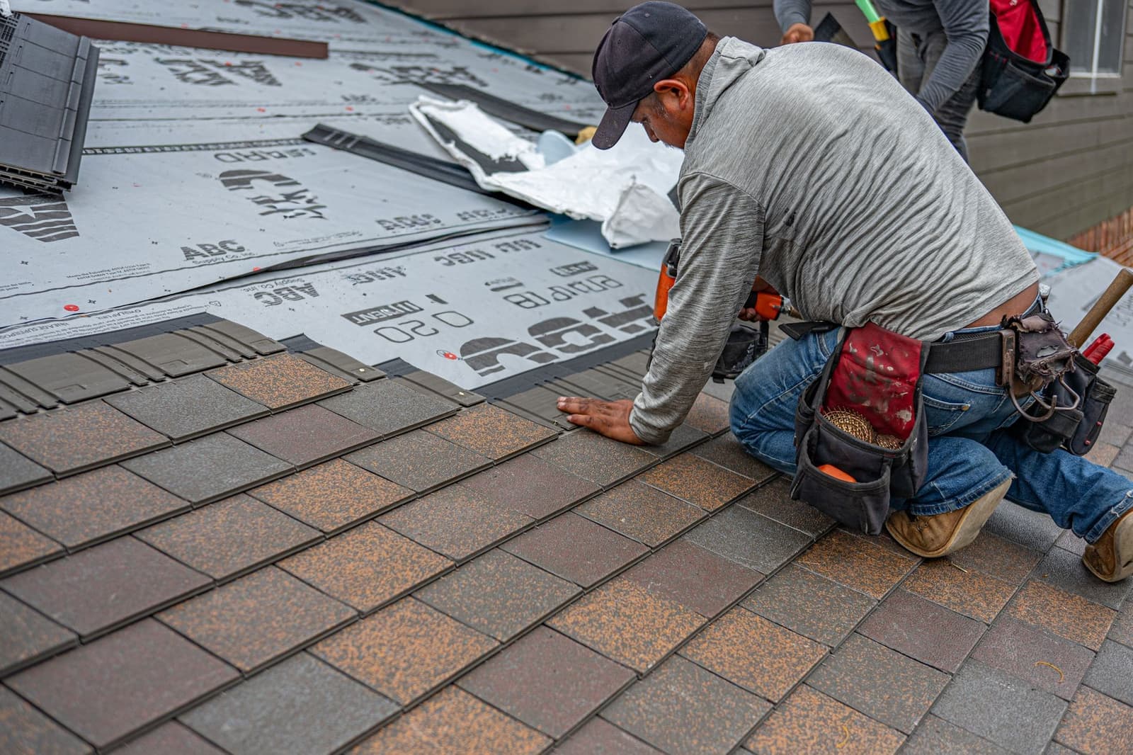 Roofer kneeling on underlayment laying asphalt shingles