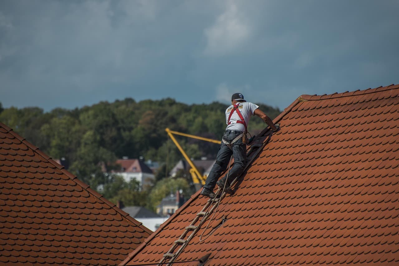 Roofer on a ladder working on a clay tile roof